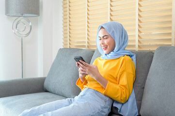 Young happy muslim woman relaxing and using smartphone in living room.