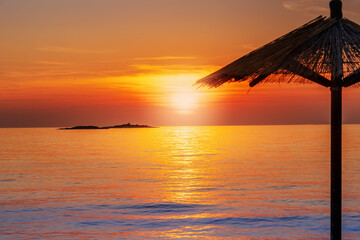 Beautiful sunset by the sea with the silhouette of a parasol and a island in background, to relax...