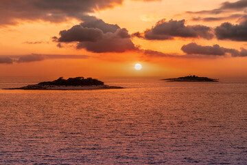 Naklejka na ściany i meble Golden Sunset into the sea with the silhouette of an island.