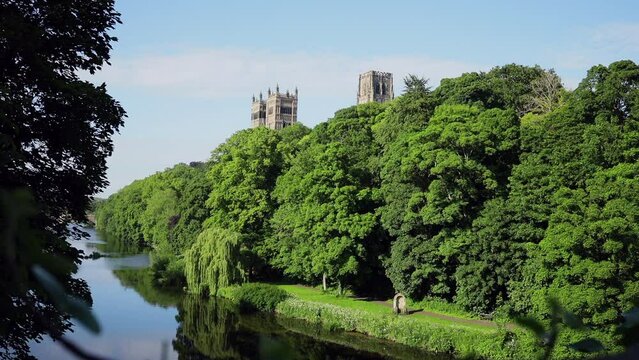 Durham England: 2022-06-07: Durham Cathedral view from the riverside (River Wear) with green trees lining the water during sunny summer day