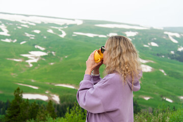 A young woman with a yellow mug in her hands looks at a plateau in the mountains. Vacation in the mountains. Nature. Early morning. Beauty.