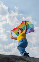 Mexican teenager waving LGBT gay pride flag on blue sky and clouds background