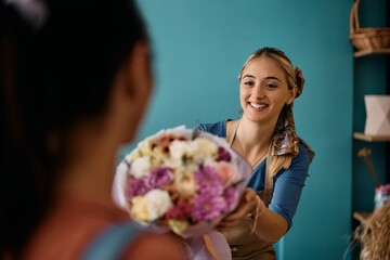 Happy female florist giving to customer bouquet of flowers at flower store.