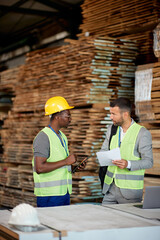 Wood warehouse owner analyzing reports with African American worker who is using digital tablet.