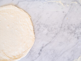 photo of traditional white pizza dough with copy space on a marble top