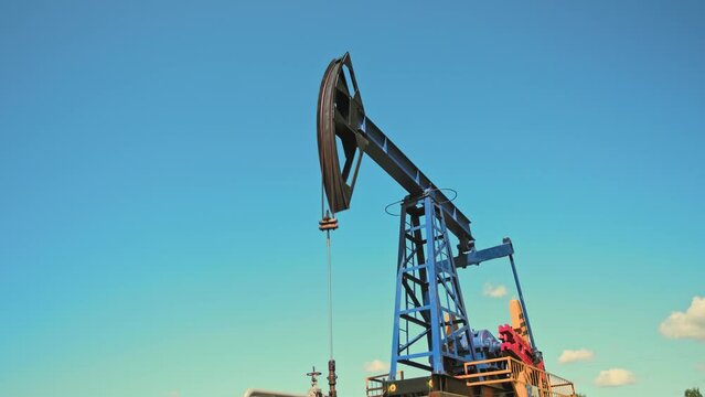 Close-up low angle shot of working oil pump rig at sunny day. Oil and gas production. Pump Jack are running. Drilling rigs for fossil fuel and crude oil production.