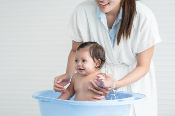 Happy Asian little baby smiling, sitting and enjoy playing water in bathtub while young mother wear bathrobe bathing her cute daughter at home. Baby bathing concept. White background