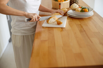 Close up of female hands sliding bread in kitchen. Baguette for breakfast.