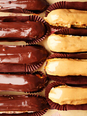 Delicious eclairs close up top view. Chocolate eclairs and creme brulee. Classic French dessert. Eclair with dark chocolate on top, filled with custard, served on pieces of dessert paper. Dessert cafe