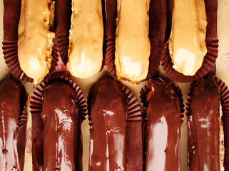 Delicious eclairs close up top view. Chocolate eclairs and creme brulee. Classic French dessert. Eclair with dark chocolate on top, filled with custard, served on pieces of dessert paper. Dessert cafe