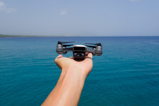 Mini drone in hand against Atlantic ocean. Close-up. Man launches drone. - Powered by Adobe