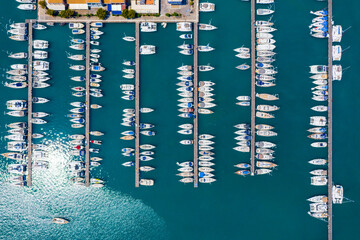 Fototapeta na wymiar Aerial top view of a lot of white boats and yachts moored in marina. Top-down view of docked sailboats. Top down view of yachts. Luxury yacht Boat in a port. Marina lot sailboat. Harbour with boats