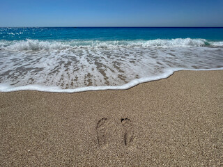 Footsteps on the sand washed by the sea waves. Barefoot steps on the beach taken by the Mediterranean sea wave. Go Everywhere