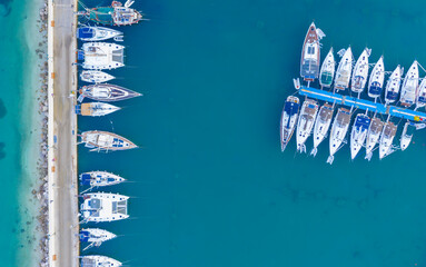 Aerial top-down view of docked sailboats. Top down view of yachts in the marina. Sailboats and regular Boats moured in Palairos Marina Greece. Sailboats and catamarans anchored in the harbour.