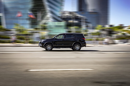 Side view rolling shot with Toyota Fortuner car in motion. Second generation crossover driving along the street in city with blurred background