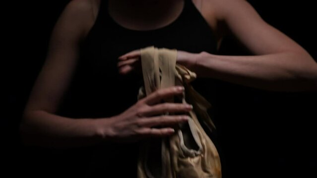 Close-up pointies in female hands at black background. Unrecognizable worried nervous Caucasian ballerina getting ready to performance