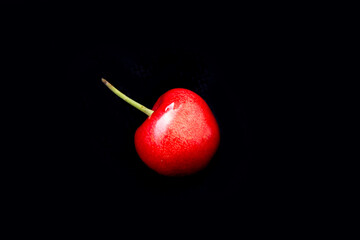 a red cherry lies on a black background