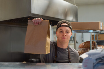 Restaurant kitchen employee holding paper bag take out food order