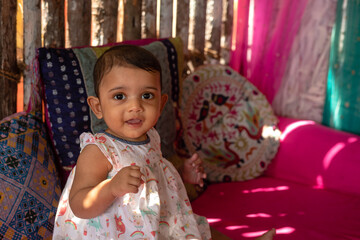 Portrait of a little adorable indian infant baby girl sitting on the bed and smiling to camera with copyspace
