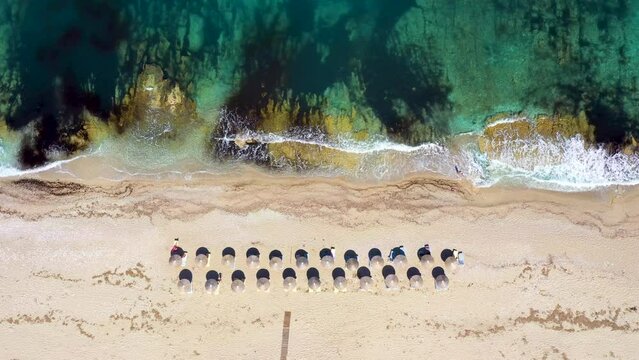 Umbrellas lined up on the sandy beach by the turquoise sea. Top view of a transparent blue sea with beautiful waves on the beach. Summer vibes concept. Exotic beach from above