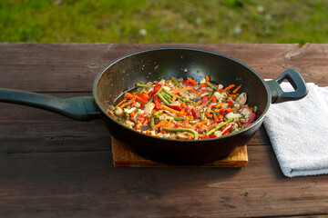 Frying pan with stewed vegetables on a napkin on a wooden table. horizontal photo