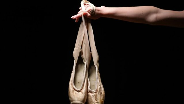 Black background with slim female hand raising pointies. Unrecognizable Caucasian young ballerina with classic dancing shoes. Art and grace concept