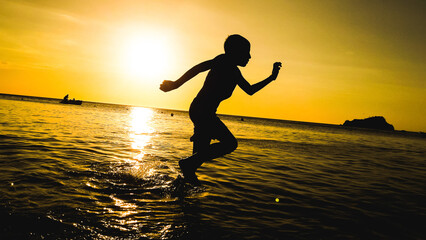 Fototapeta na wymiar silhouette of boy running on the beach at sunset