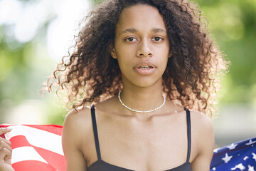 Young African american woman is waving American flag on top of at nature background. USA resident, US citizen. Immigration concept