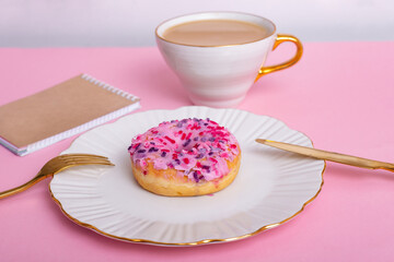 Pink donut on plate, golden colored knife and fork, cup of coffee, with copy space
