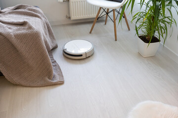 Robotic vacuum cleaner on laminate wood floor in bedroom.