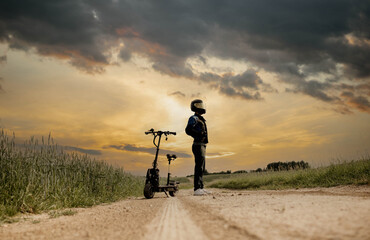 Male extreme driver in a helmet on an electric scooter off-road at sunset. The concept of electric transport in the village.