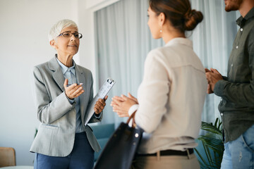 Obraz premium Mature real estate agent talking to young couple in her office.