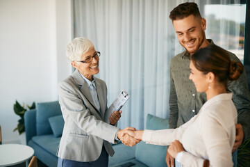 Obraz premium Happy senior financial advisor shaking hands with young couple after successful meeting in the office.