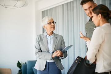 Mature real estate agent communicating with couple during meeting in her office.