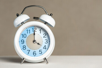 Four hours on the alarm. A white alarm clock is on a white table. The clock hand points to 4...