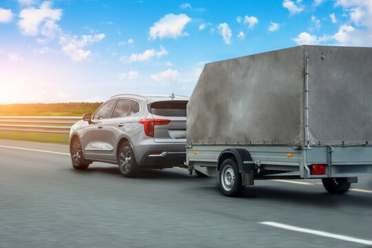 Car with a trailer covered with an awning is driving along the highway in the sky clouds and sunset.