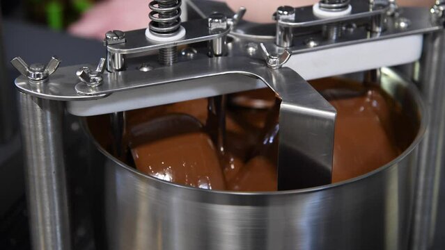 The process of making chocolate confectionery. Stirring machine mixes brown chocolate mass. Small business. Real time video. Selective focus. Small confectionery production theme.