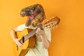 Unrecognizable woman playing guitar wearing dinosaur animal mask isolated on studio orange background