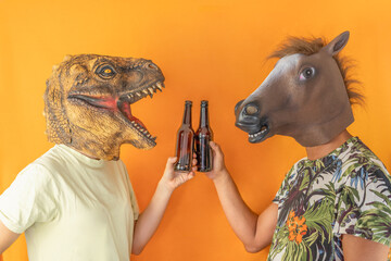 Funny couple of friends having fun toasting beer bottles wearing horse and dinosaur animal mask...