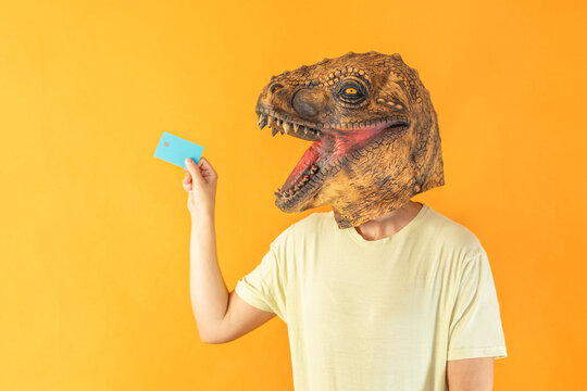 Portrait Of Young Woman In Dinosaur Animal Head Mask Holding Credit Card On Orange Background