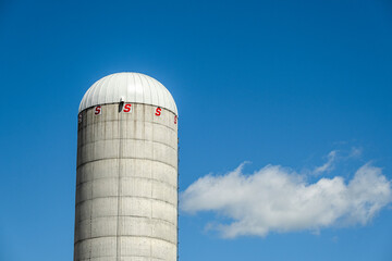 A concrete grain silo against a blue sky and a cloud.  Access to grains is difficult causing food shortages and high inflation around the world.