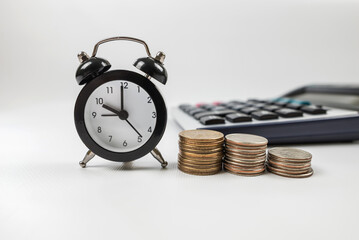 stacks of coins with alarm clock and calculator on white.