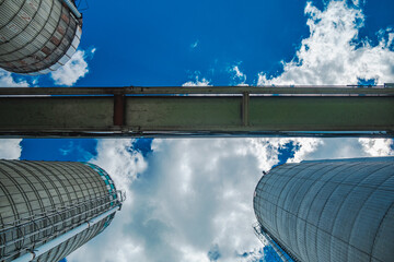Three concrete grain silos against a blue sky and clouds.  Access to grains is difficult causing food shortages and high inflation around the world. 