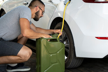 A young man steals gasoline from the gas tank in the white car. A young man pumps gasoline from a...