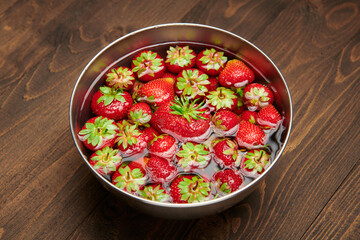 a full bowl of strawberries in water, dark wooden background, concept of fresh fruits and healthy food