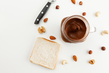 A jar of chocolate paste, bread, a knife and various types of nuts. Cashew, almond, walnut, hazelnut, isolated on white background.