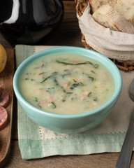 Traditional portuguese green soup in a bowl with bread slices and wine over wooden table