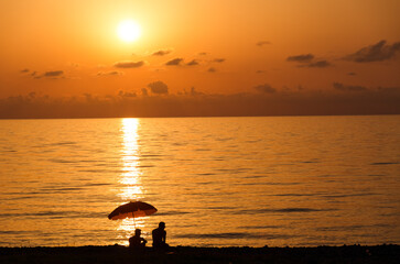 Two silhouettes of a man under a beach umbrella on the seashore at sunset