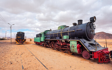 Old unused steam and diesel locomotive train at Wadi Rum train station, sandy desert around