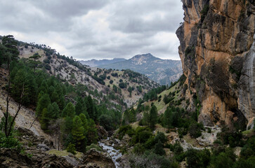 Fototapeta na wymiar mountain landscape with a river in the center and the steep mountain on the right, on a cloudy autumn day. Borosa River, Sierra de Segura, Spain